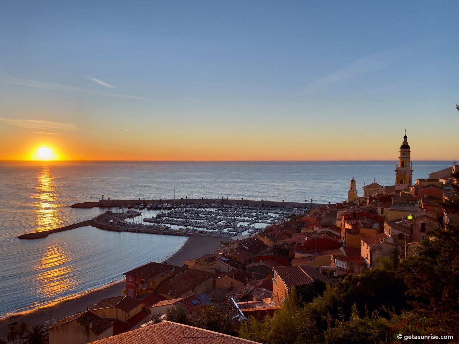 Winter sunrise over the sea seen from the old town of Menton, with the harbour and the bell tower of Saint-Michel church