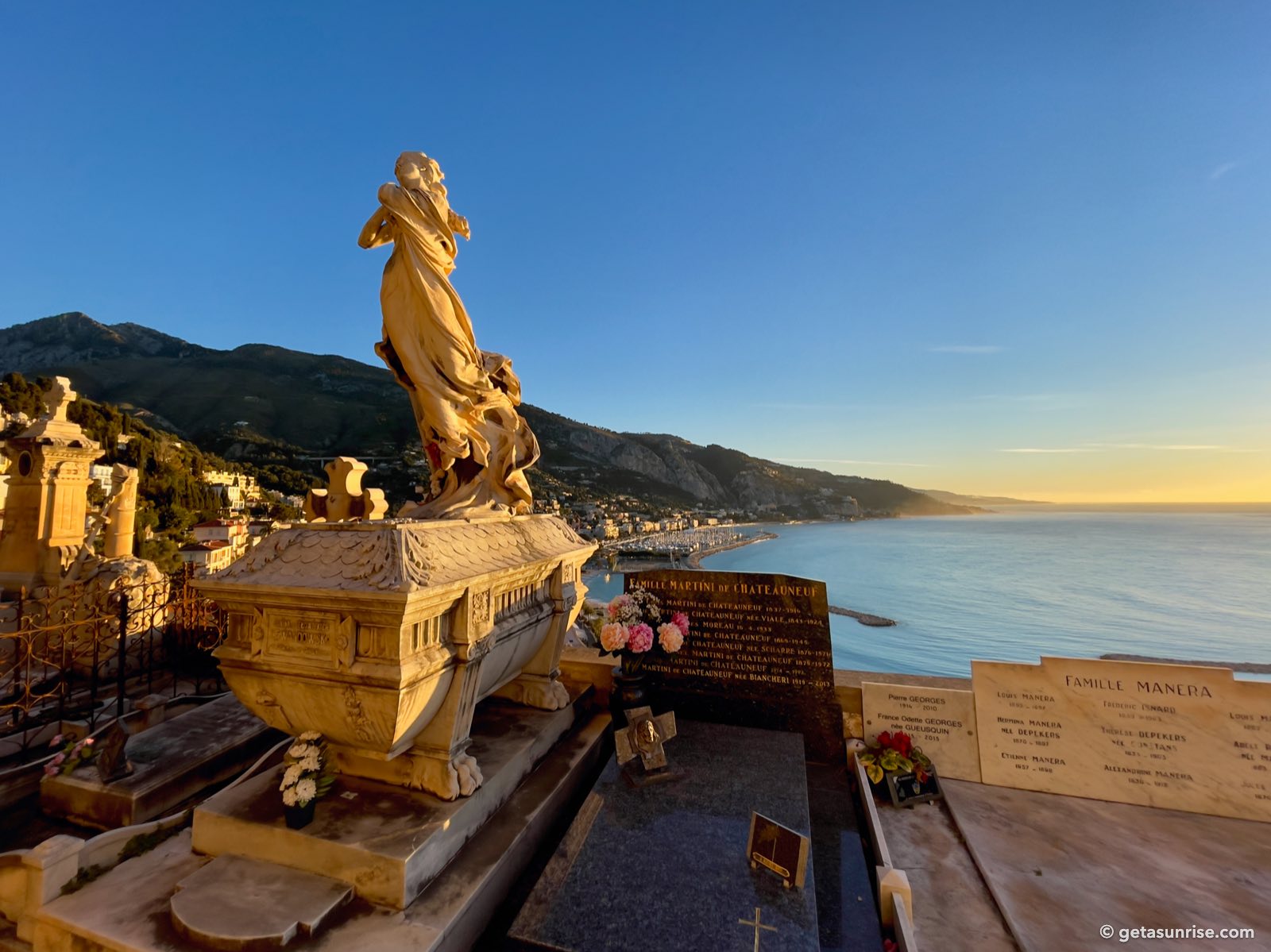 Morning light on a gilded statue in the old cemetery of Menton, with the coast towards Italy and the sea in the background