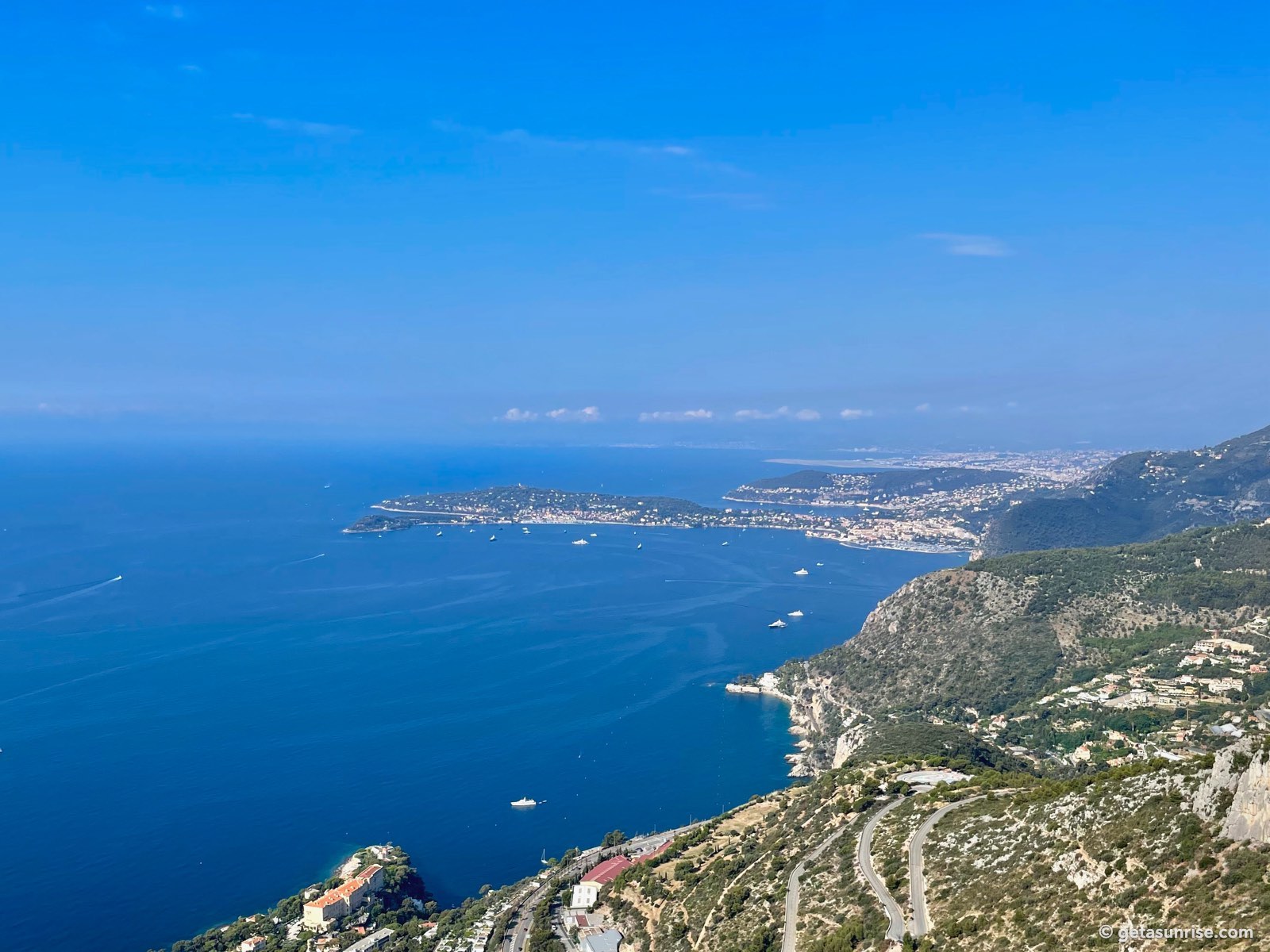 The coast seen from high above Cap d’Ail, with the winding roads of La Turbie, Cap Ferrat, Villefranche-sur-Mer and Nice under a blue sky