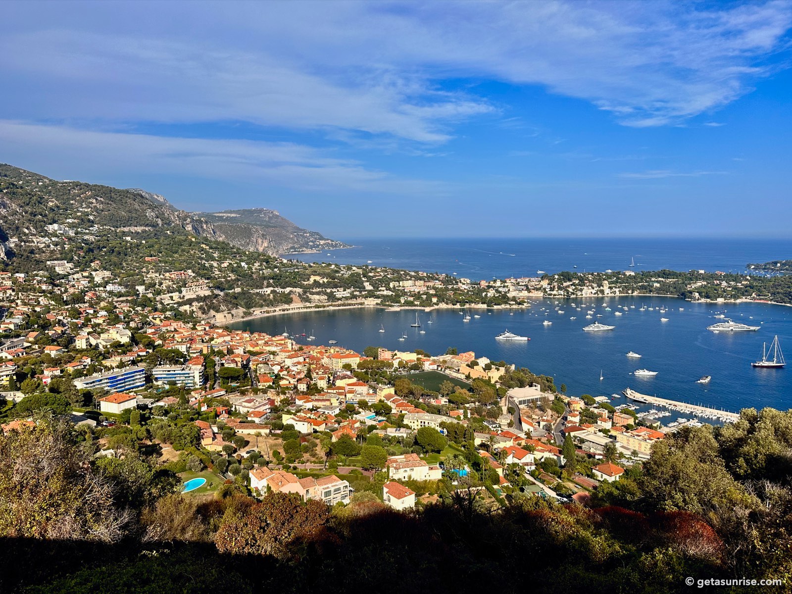 The bay of Villefranche-sur-Mer seen from above, with the old town, anchored boats, Cap Ferrat and the mountains towards Èze